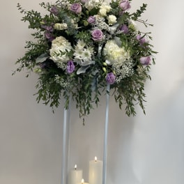 Lavender and white floral arrangement on a tall stand with candles below