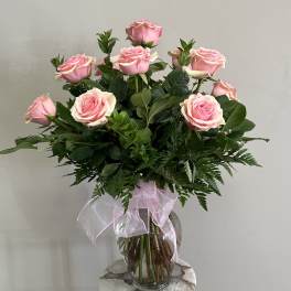 Pink roses arranged in a clear glass vase with a pink ribbon bow