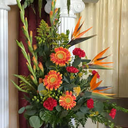 Tall arrangement of orange gerberas, red carnations, and birds of paradise in a black urn vase