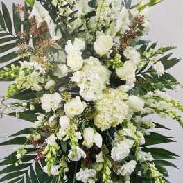 Large white floral standing spray with cascading blooms and dark palm leaves