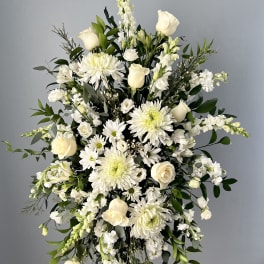 Tall standing spray of white roses, daisies, and snapdragons on a metal easel.