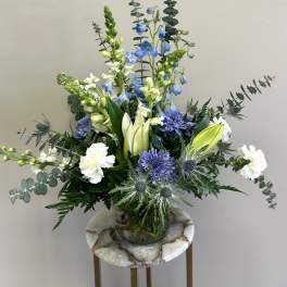 Arrangement of blue and white flowers with lilies and carnations in a clear glass vase