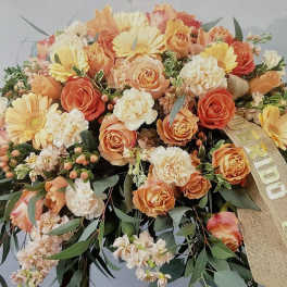 Orange and cream roses, carnations, and gerberas in a large spray with a burlap sympathy ribbon