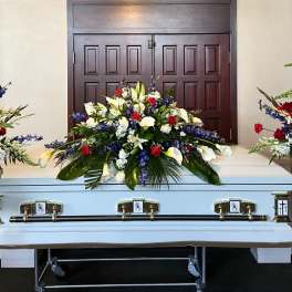 White casket with red, white, and blue funeral flower sprays