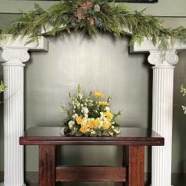 Yellow and white floral arrangements on pedestals beneath a white arch.