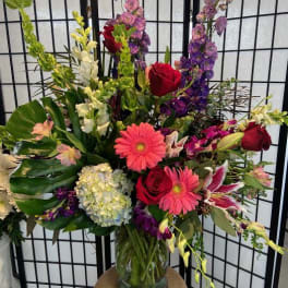 Mixed bouquet in a glass vase with red roses, pink gerberas, and purple flowers
