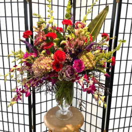 Large mixed flower arrangement in a clear glass vase on a stool