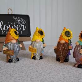 Four small gnome figurines holding sunflowers and welcome signs