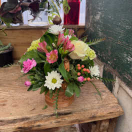 Mixed flower arrangement in a small wicker basket with pink, white, and cream blooms