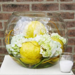 White hydrangeas and yellow decorative gourds in a glass bowl