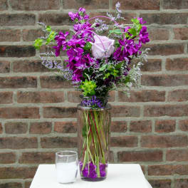 Purple floral arrangement in a tall glass vase with a white rose