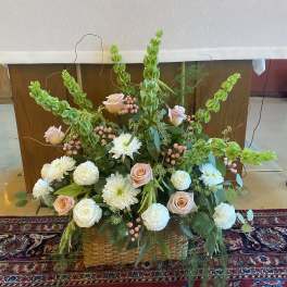 Large floral arrangement with pale roses, white blooms, and green spikes in a woven basket