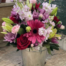 Mixed pink and red flowers arranged in a metal bucket