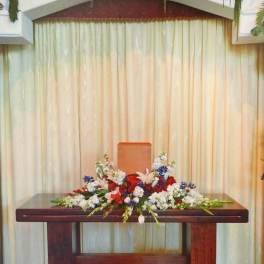 Symmetrical floral altar display with red, white, and blue flowers in white urns
