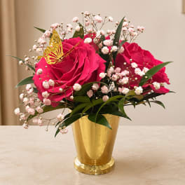 Pink roses in a gold vase with baby's breath and a butterfly accent