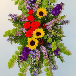 Tall standing floral spray with sunflowers, red roses, and purple blooms