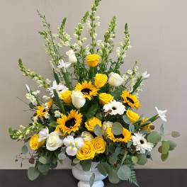 Tall yellow and white arrangement with sunflowers, roses, daisies and snapdragons in a white pedestal vase
