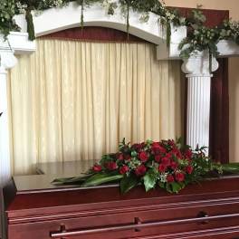 Red and orange floral sprays around a casket in a funeral setting