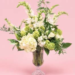 Cream and green floral arrangement in a clear pedestal vase