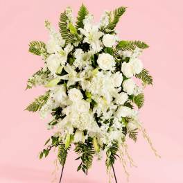 White floral standing spray with roses and lilies on a pink background