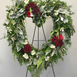 Heart-shaped floral wreath with red roses and white flowers on a stand