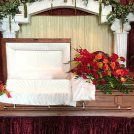 Casket spray with red and orange flowers beside matching potted plants