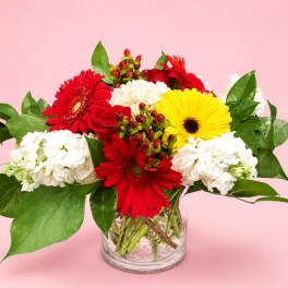 Mixed bouquet of red, yellow, and white flowers in a clear glass vase