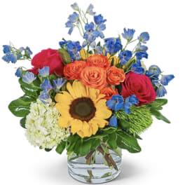 Mixed bouquet with sunflowers, roses, and blue flowers in a glass vase