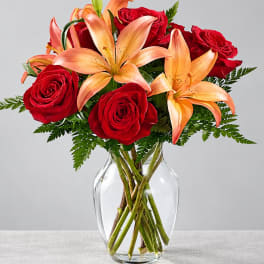 Red roses and peach lilies in a clear glass vase