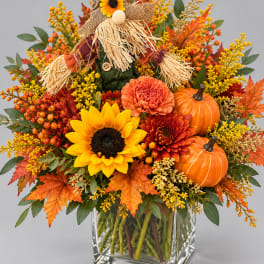 Fall bouquet with sunflowers, roses, mums, pumpkins, and a scarecrow in a glass vase
