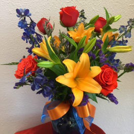 Bouquet of red roses, yellow lilies, and blue flowers in a vase
