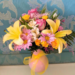 Pink and yellow flower arrangement in a pink vase with a yellow ribbon