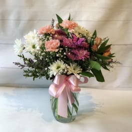 Mixed bouquet of pink, white, and peach flowers in a glass vase with a pink ribbon
