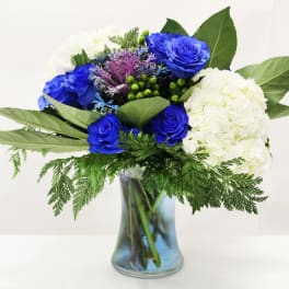 Blue roses and white hydrangeas with greenery in a clear glass vase with blue-tinted water