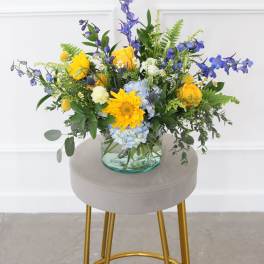Mixed bouquet in a clear glass vase with yellow, blue, and white flowers