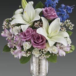 White lilies and lavender roses in a glass vase with blue flowers