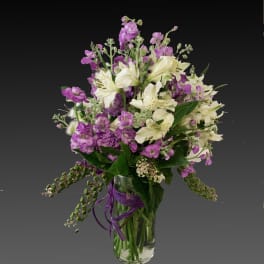 Purple and white flowers arranged in a clear glass vase with a ribbon