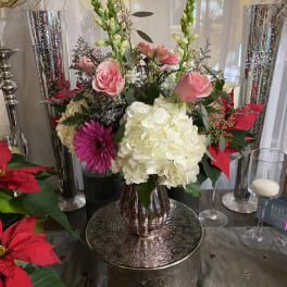 Pink roses and white hydrangeas in a metallic vase with red poinsettias nearby.