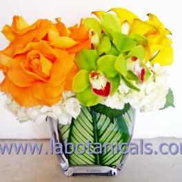 Orange roses, green orchids, and yellow blooms in a clear vase