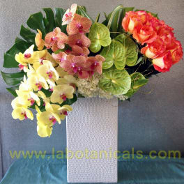 Tropical floral arrangement with orchids and roses in a white vase
