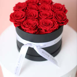 Red roses arranged in a black round box with a white ribbon