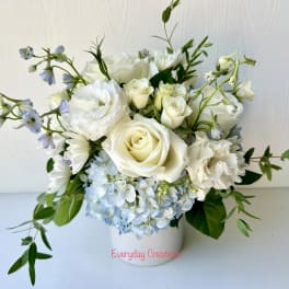 White roses and pale blue hydrangeas in a white vase