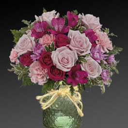 Pink and magenta flower arrangement in a green glass vase with a ribbon bow