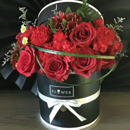 Red roses and carnations in a black hatbox with a white ribbon