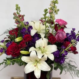 Bouquet of white lilies, red and pink roses, and purple flowers in a dark vase