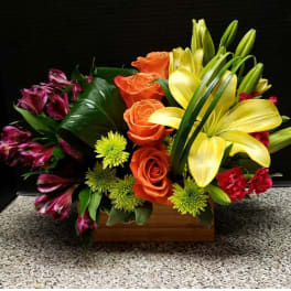 Mixed bouquet with yellow lilies, orange roses, and purple alstroemeria in a wooden box