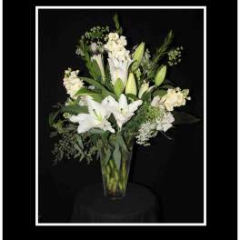 White lilies and mixed white flowers in a tall glass vase