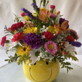 Colorful mixed flower arrangement in a yellow smiley-face vase