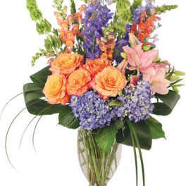 Mixed bouquet of orange roses, purple flowers, and pink lilies in a glass vase