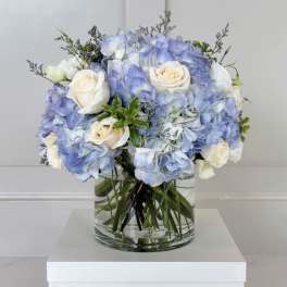 Blue hydrangea and white rose bouquet in a clear glass vase